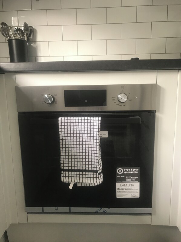 A kitchen with a built-in oven, a control panel, and a black oven mitt hanging on the door.