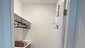 A small, enclosed room with a bunk bed, a shelf with clothes, and a coat rack.