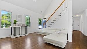 Ein geräumiges Wohnzimmer mit einem großen, weißen Modulsessel, einer Holztreppe und einem Oberlicht.