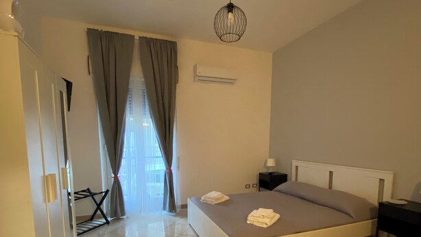 Une chambre à coucher comprenant un lit, une table de chevet, une lampe, un appareil de climatisation et une fenêtre avec des rideaux.