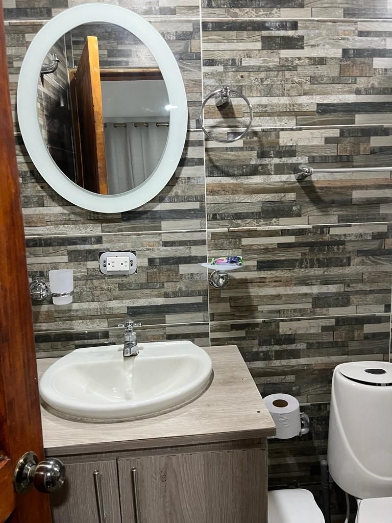 A bathroom with a wooden vanity, a round mirror, a sink, a toilet, and a wall-mounted towel rack.