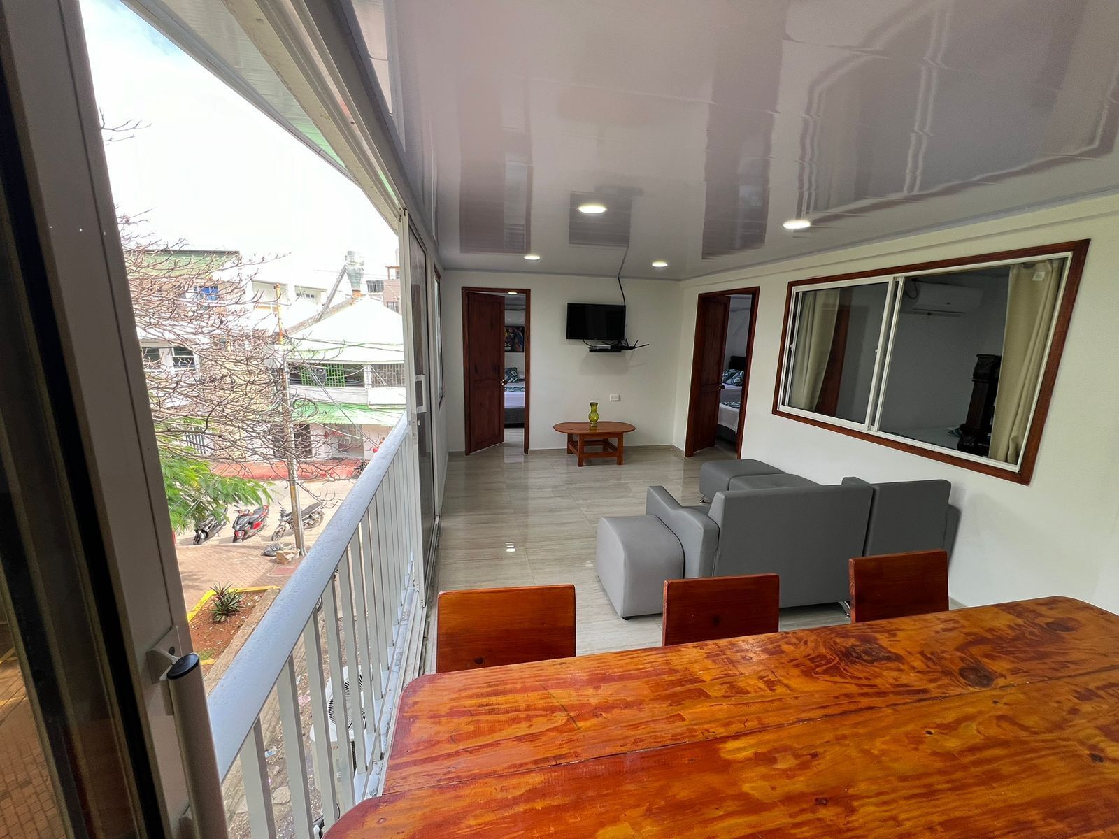 A balcony with a wooden table and chairs, a grey sofa, and a TV mounted on the wall.