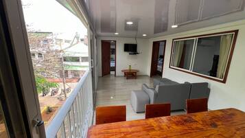 A balcony with a wooden table and chairs, a grey sofa, and a TV mounted on the wall.