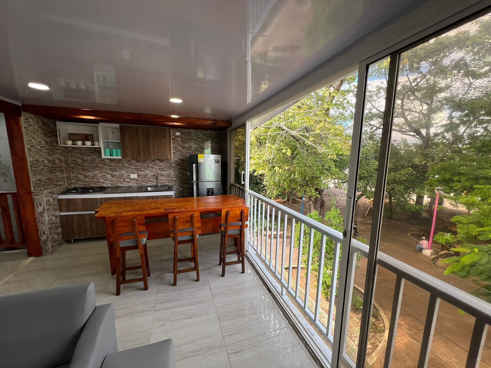 A modern kitchen with a stone backsplash, a stainless steel refrigerator, and a wooden dining table with four chairs.