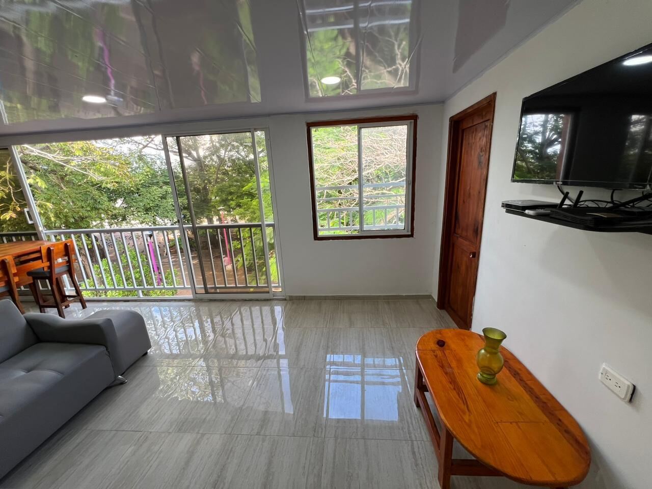 A spacious living area with a grey sofa, a wooden table, and a TV mounted on the wall.
