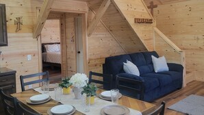 Een houten interieur met een eettafel gedekt voor vier personen, een blauwe bank en een trap naar een hoger niveau.