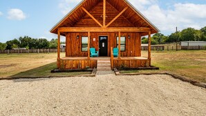 Een houten chalet met een schuin dak en een veranda, plus twee blauwe Adirondack stoelen.