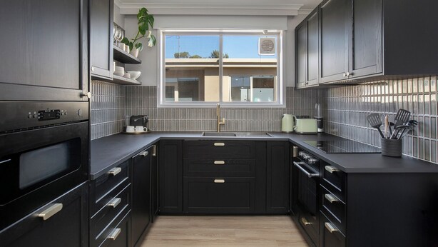 A modern kitchen with dark cabinetry, a window, and a view of a building outside. - Enjoy a Luxurious Elwood Escape (Elwood)