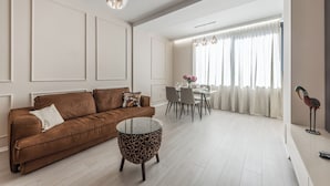 Una sala moderna con un sofá marrón, una mesa de centro de vidrio y un comedor con una mesa y sillas blancas.
