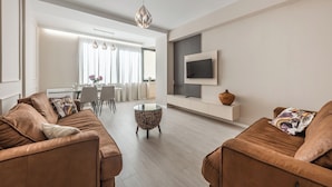 Una sala de estar moderna con un sofá de cuero marrón, una mesa de centro de vidrio y una zona de comedor con una mesa y sillas blancas.
