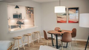 A modern kitchen with white cabinets, a microwave, and a built-in oven. There is a dining area with a round wooden table and six chairs.