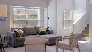 A modern living room with a grey sofa, two armchairs, a floor lamp, and a staircase.