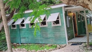 A small, green wooden cabin with multiple windows and a porch area.