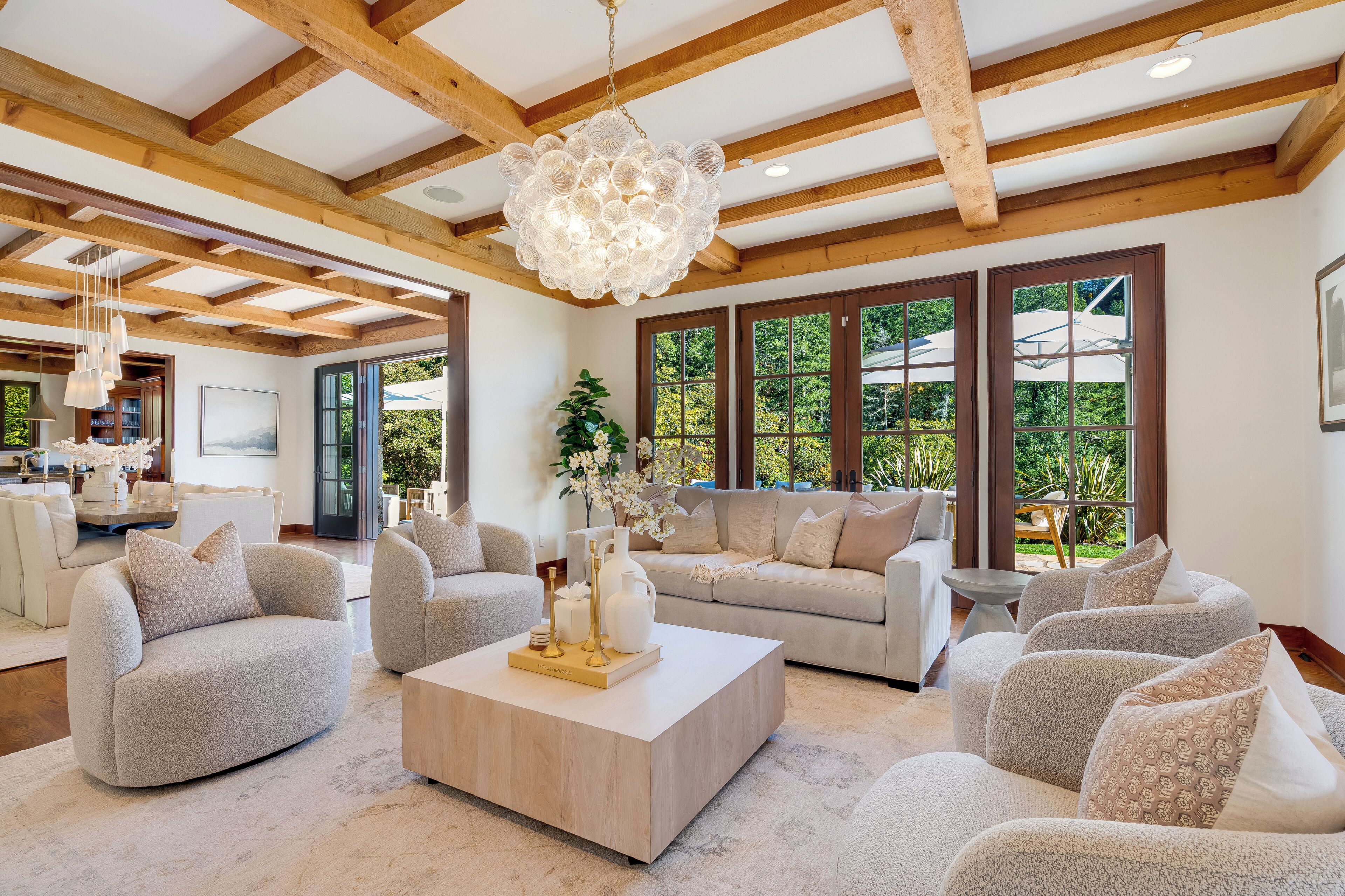 A spacious living room with a high ceiling, large windows, and a modern chandelier.
