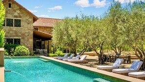 A swimming pool with lounge chairs, a stone building, and olive trees. - Luxury 38-Acre Calistoga Mansion - Pool, Vineyard, Amazing Views, Boccee & More (Calistoga)