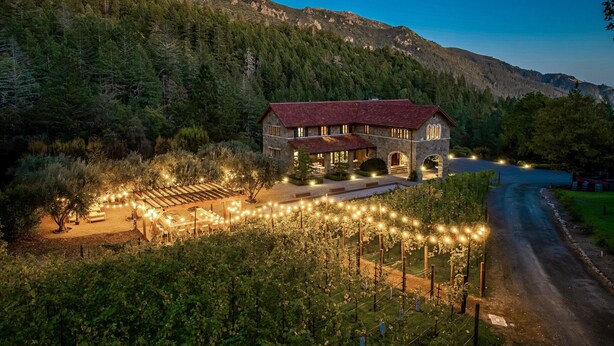 A stone building with a red roof, surrounded by a vineyard and a forested mountain backdrop. - Luxury 38-Acre Calistoga Mansion - Pool, Vineyard, Amazing Views, Boccee & More (Calistoga)