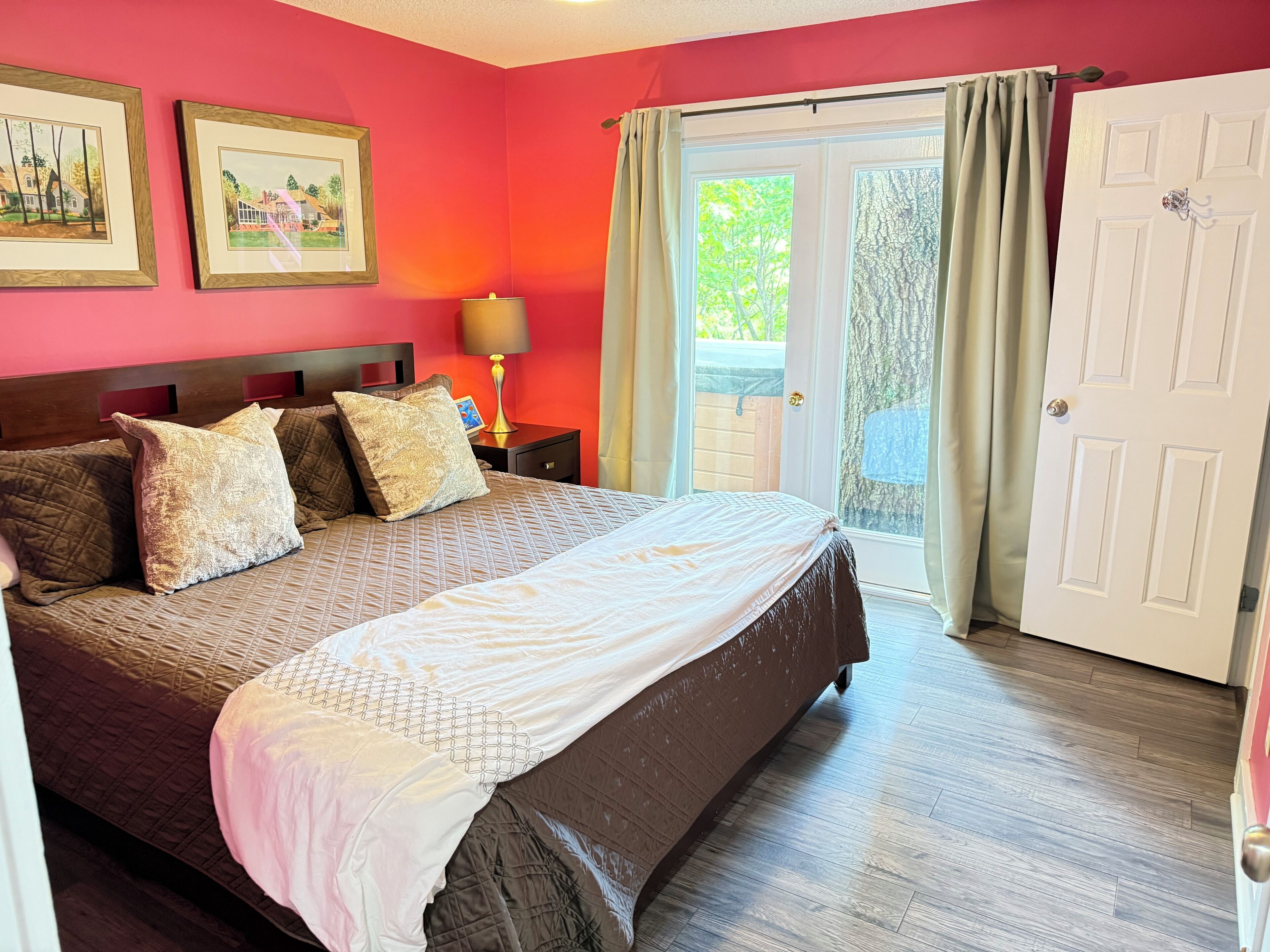 A bedroom with a large bed, a nightstand with a lamp, and a door leading to a balcony.