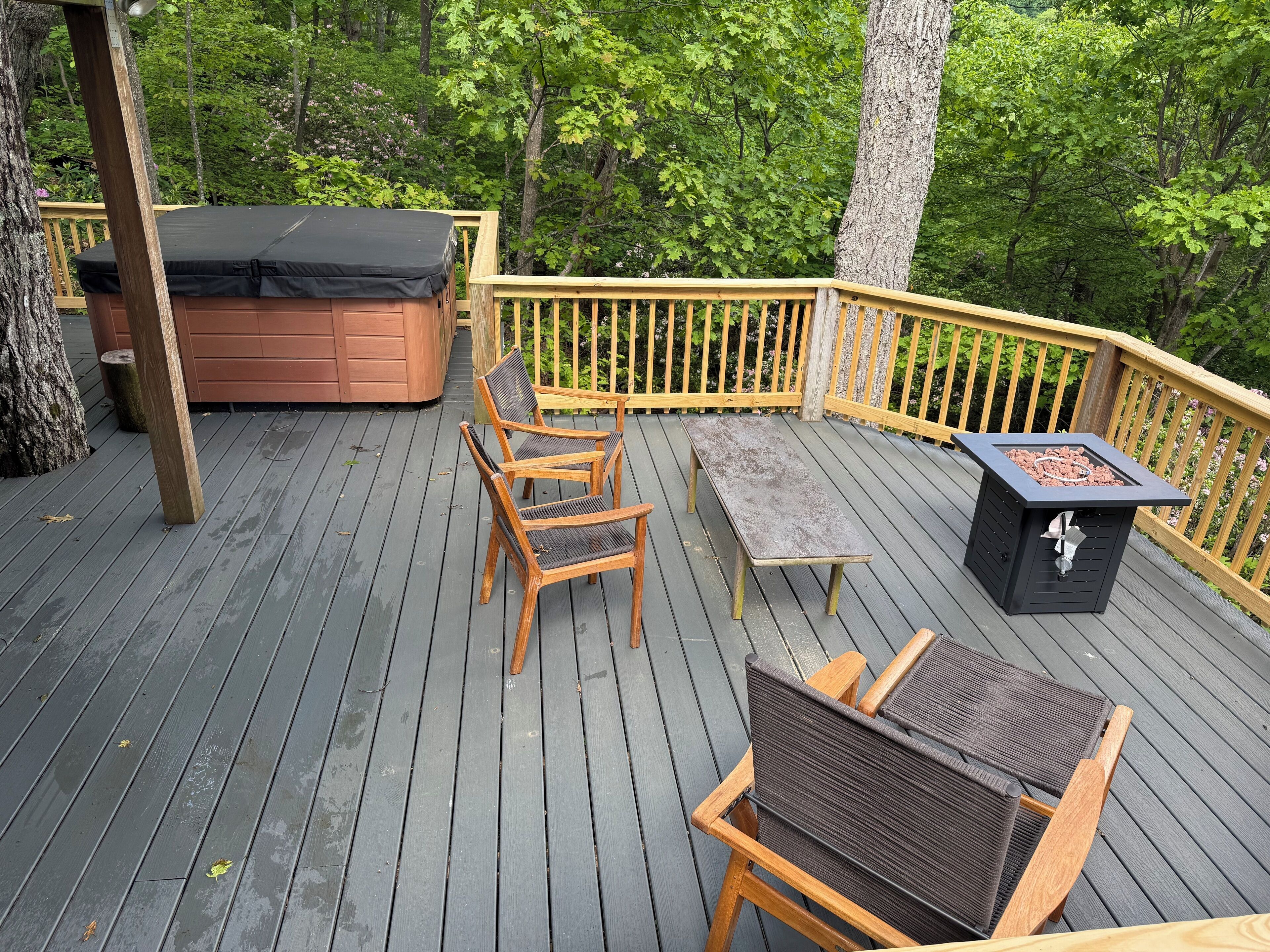 Une terrasse en bois avec un jacuzzi, des chaises en bois, une table et un foyer extérieur.