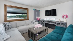 A living room with a gray sectional sofa, a teal couch, a wooden coffee table, and a flat-screen TV mounted on the wall. - Freshly Renovated 4 BR Lake House, 2 Docks, Free Kayaks, 2 Fire Pits (Dry Ridge)