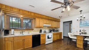 A modern kitchen with wooden cabinets, a dishwasher, a stove, and a bar area with stools. - Freshly Renovated 4 BR Lake House, 2 Docks, Free Kayaks, 2 Fire Pits (Dry Ridge)