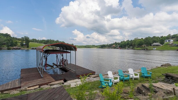 A wooden dock with a covered seating area and several Adirondack chairs by a calm lake. - Freshly Renovated 4 BR Lake House, 2 Docks, Free Kayaks, 2 Fire Pits (Dry Ridge)