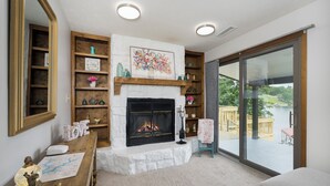 A cozy living room with a fireplace, wooden shelves, and a large window overlooking a deck. - Freshly Renovated 4 BR Lake House, 2 Docks, Free Kayaks, 2 Fire Pits (Dry Ridge)