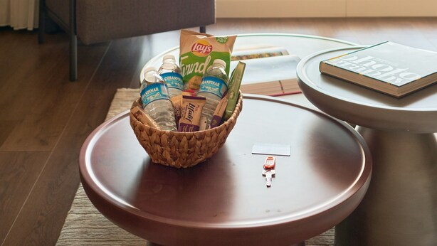 Een kamer met uitzicht op een stadslandschap, een stoel, een tafel met een mand lekkernijen en een boek.