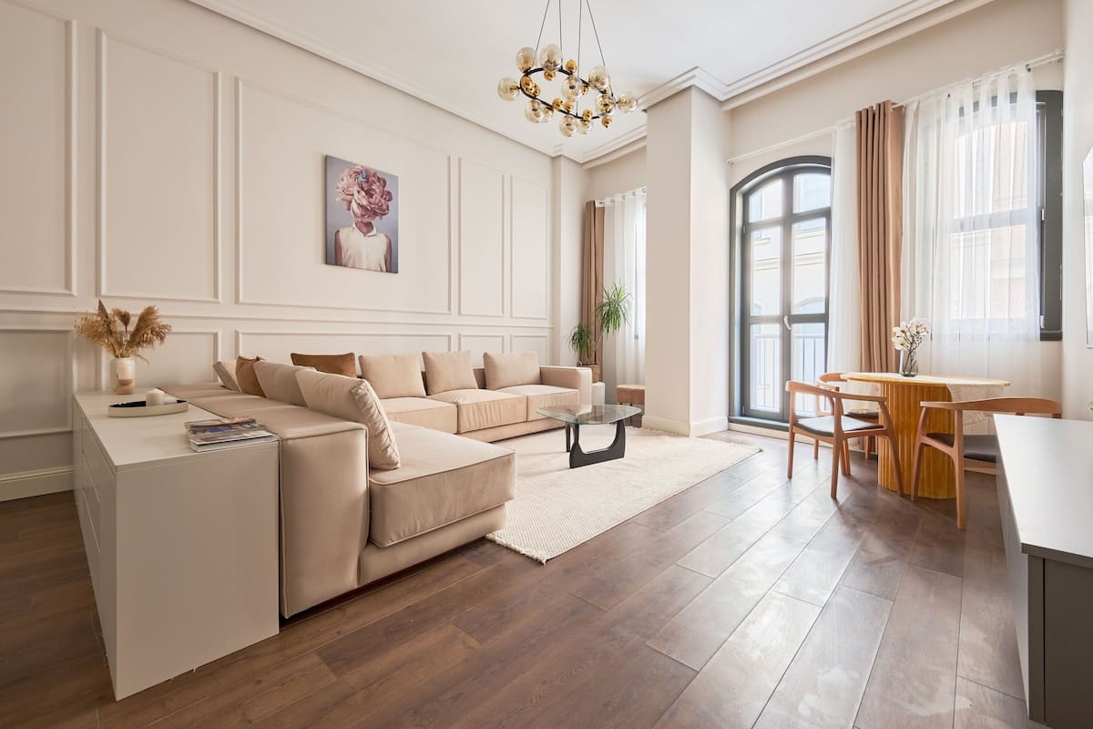 Una sala de estar moderna con un sofá color beige, una mesa de centro de vidrio y un comedor con sillas y mesa de madera.