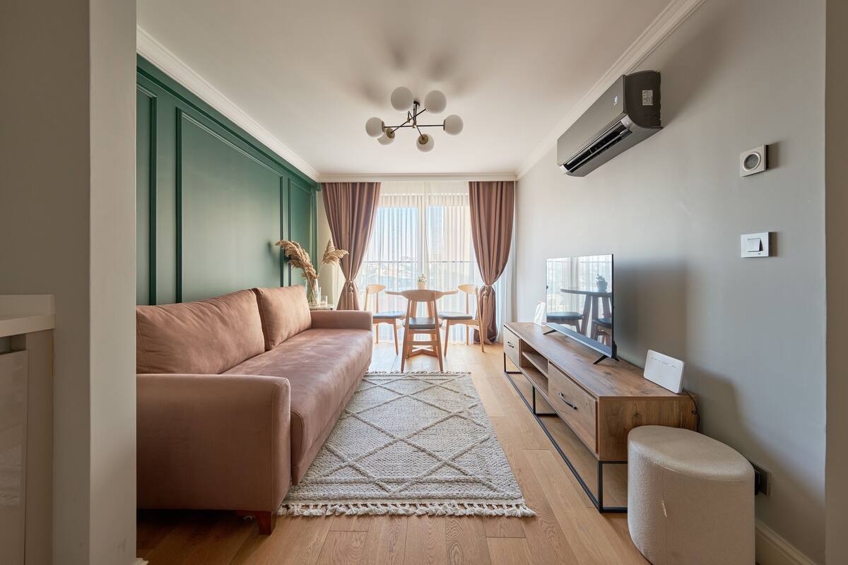 Una sala de estar con un sofá, una mesa de centro, un televisor y un pequeño reposapiés.
