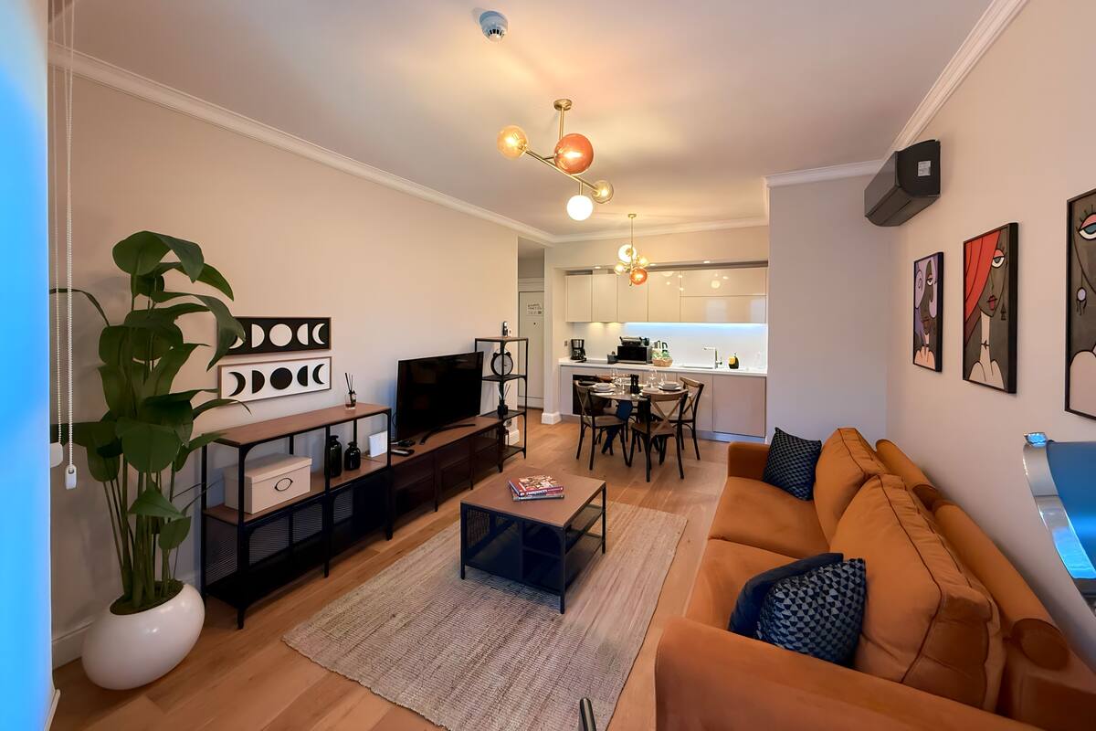 Una sala de estar moderna con televisor, sofá, mesa de centro y un comedor con sillas y una mesa.