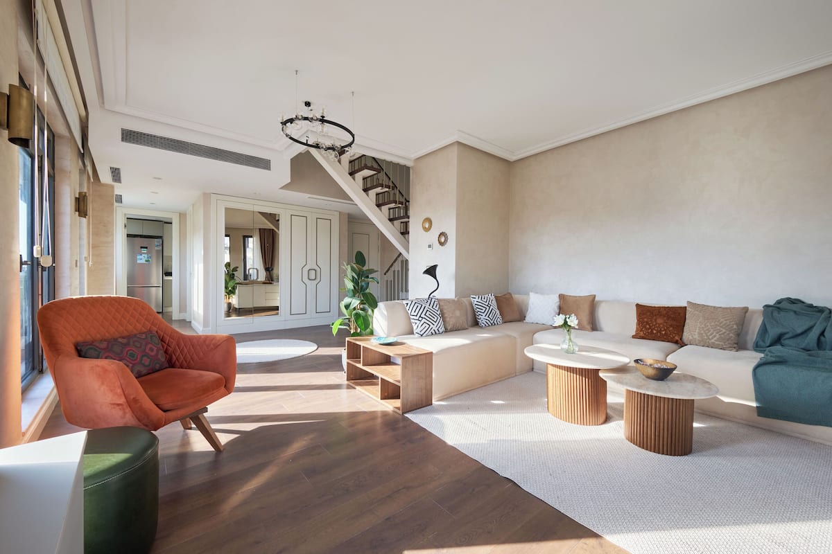 Una sala de estar moderna con una escalera, un conjunto de sofá, una mesa de centro de madera y un sillón estampado.