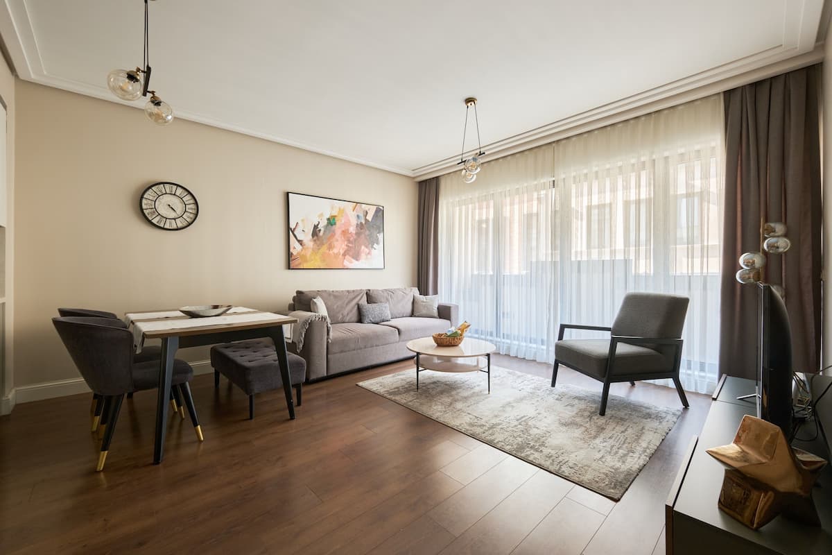 Una sala de estar moderna con un sofá, una mesa de comedor con sillas, una mesa de centro y un amplio ventanal con cortinas.