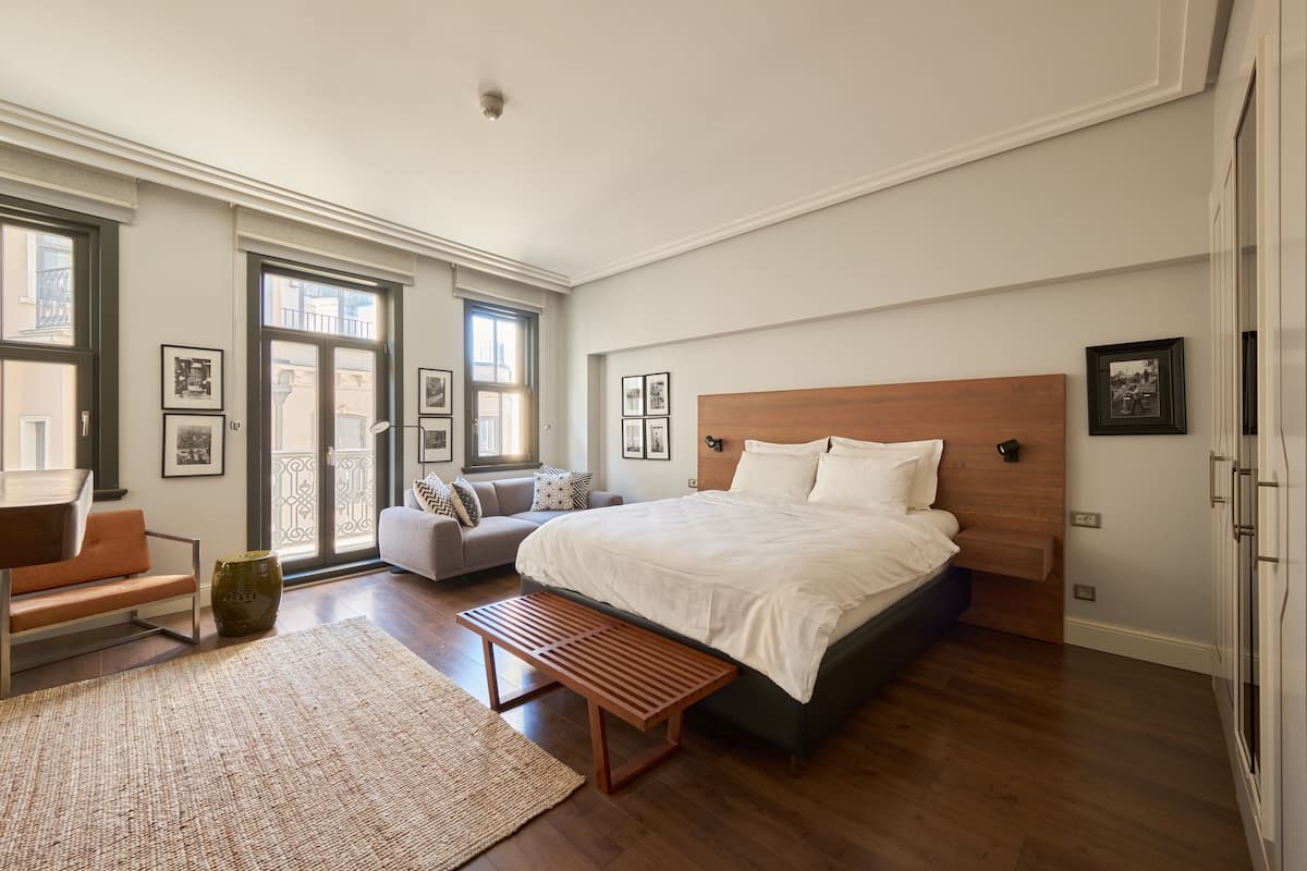 Un dormitorio con una cama grande, una banca, un sofá y una mesa de comedor.