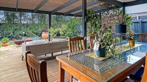 An outdoor dining area with a glass table, wooden chairs, and a pergola overhead. - Mani Manor - Linen Included (Cowes)