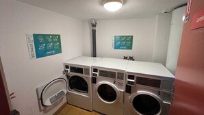 Une buanderie équipée de trois machines à laver, d’un sèche-linge et de deux panneaux d’affichage fixés au mur, indiquant les instructions.