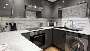 A modern kitchen with grey cabinets, a built-in oven, a microwave, and a washing machine.