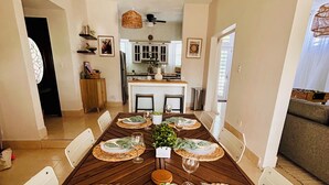 Comedor con una larga mesa de madera dispuesta para seis comensales, flanqueada por sillas blancas.