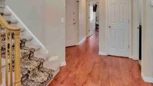 A hallway with wooden flooring, white walls, and a staircase with patterned carpet. - Great location for your Aurora visit (Aurora)