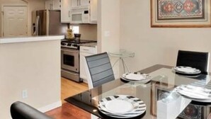 A modern kitchen with white cabinets, stainless steel appliances, and a glass dining table set for four. - Great location for your Aurora visit (Aurora)