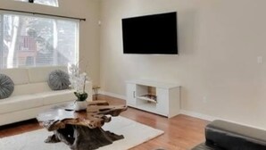A modern living room with a white sofa, a coffee table with a tree stump centerpiece, a flat-screen TV mounted on the wall, and a white console table. - Great location for your Aurora visit (Aurora)