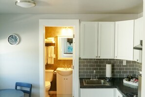 Een kleine keuken met een spoelbak, aanrecht en kastjes. Op de muur hangt een klok.
