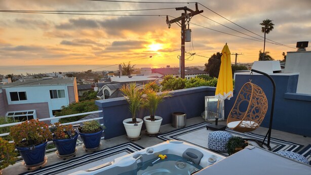 Eine Dachterrasse mit Whirlpool, Blumentöpfen, einer Hängematte und Blick auf den Sonnenuntergang über der Stadt.