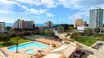 A hotel with a swimming pool, a tennis court, and a parking area.