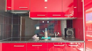 A modern kitchen with red cabinetry, a stainless steel sink, and a black countertop. - PRAIA DA ROCHA - PARAISO SOL II (Portimão)