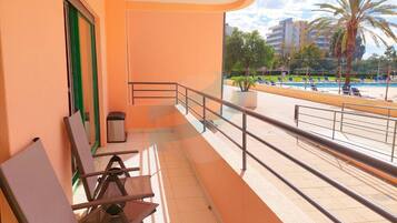 A balcony with a view of a pool and palm trees, a trash bin, and a green door.