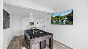 Une table de billard dans une pièce dotée d’un plancher en bois, de murs blancs et d’un tableau représentant une cascade.