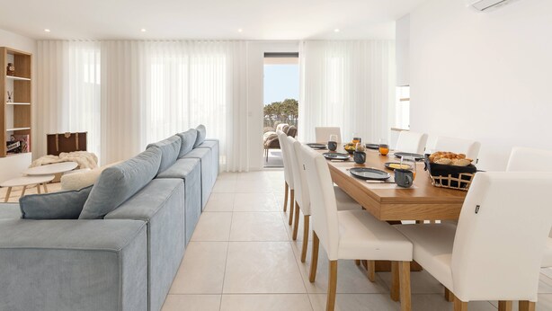 En moderne stue med sofa, spisebord og stole. Store vinduer giver udsigt til det fri.