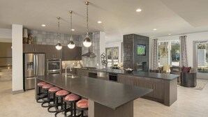 Une cuisine moderne dotée d’un grand îlot central, d’appareils électroménagers en acier inoxydable et d’un téléviseur fixé au mur.