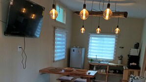 A cozy living room with a wooden floor, a round stone table, a television mounted on the wall, and hanging pendant lights. - El roble cabins (Caburgua)