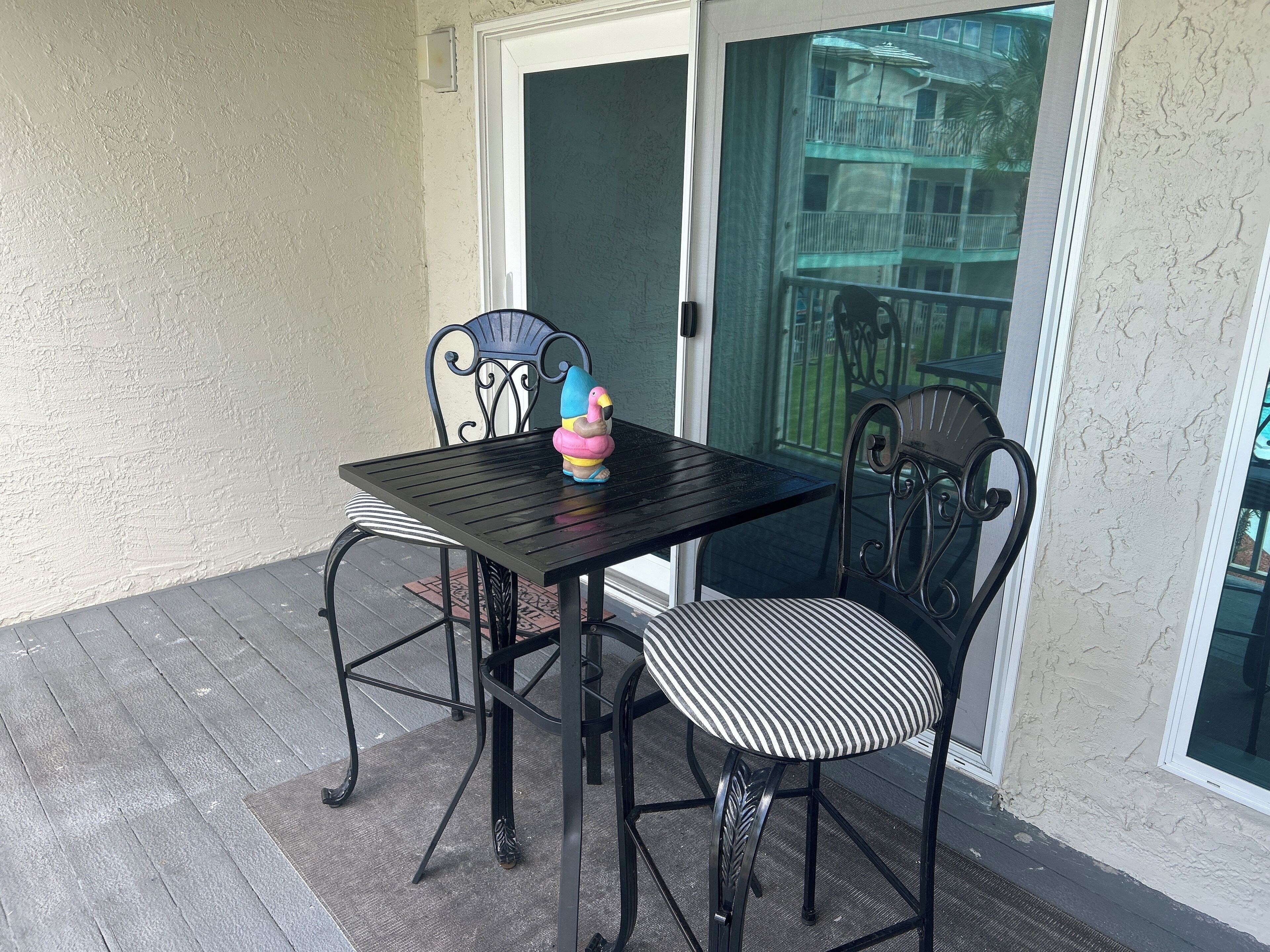 A patio with a black metal table and chairs, a decorative flamingo, and a view of a building through a glass door.